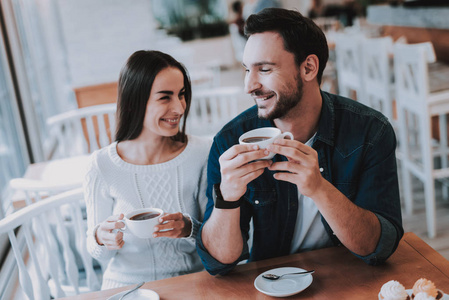 一对夫妇在咖啡馆里休息。 夫妻是美丽的年轻男女。 夫妇正在喝茶。 人们互相看着对方。 人们坐在桌子旁。 人们快乐而微笑。 白天。