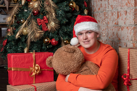 帅哥抱着熊坐在树下，周围是礼物
