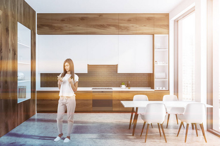 女性在现代厨房的内部，黑色砖墙，混凝土地板，木制台面和白色橱柜，白色和木制橱柜在左边。 带椅子的白色桌子。 调色图像