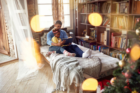 非洲裔美国人的父亲和可爱的女儿为圣诞假期阅读童话故事
