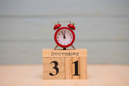12月31日设置在木制日历和红色闹钟与蓝色背景。 钟展5分钟到午夜