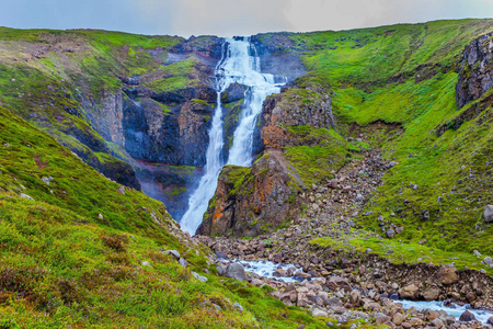 寒冷多雨的七月在冰岛。 强大的瀑布流落下，咆哮声在裂口中落下。 积极和极端旅游的概念