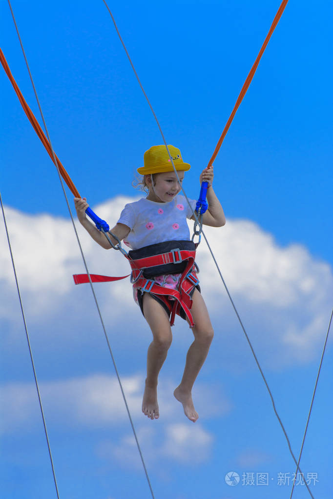 一个小女孩在蹦床上跳得很高蹦床上用橡胶绳抵着蓝