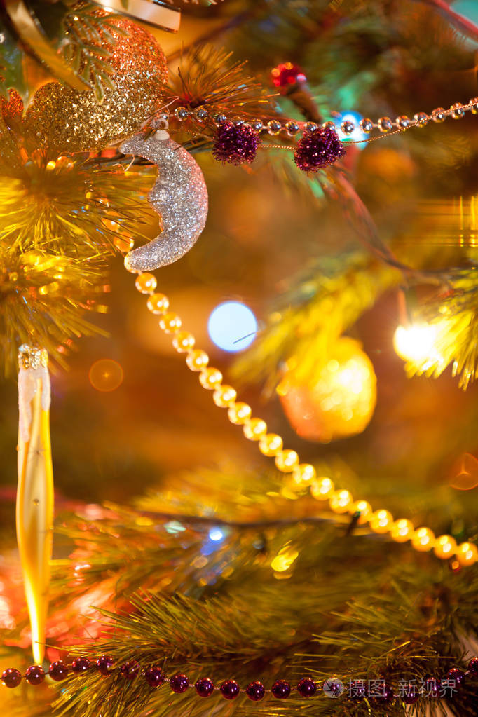 金色花环由小球挂在绿色云杉圣诞树树枝上特写。围绕着模糊的灯光和球