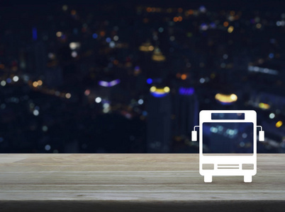 木制桌子上的公共汽车平面图标，模糊了现代城市塔楼和摩天大楼商业运输服务理念的绚丽夜景