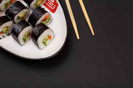 寿司卷在诺里海藻床单与鳄梨和红鱼在陶瓷板和木棒。 带有黑色背景的顶部视图。