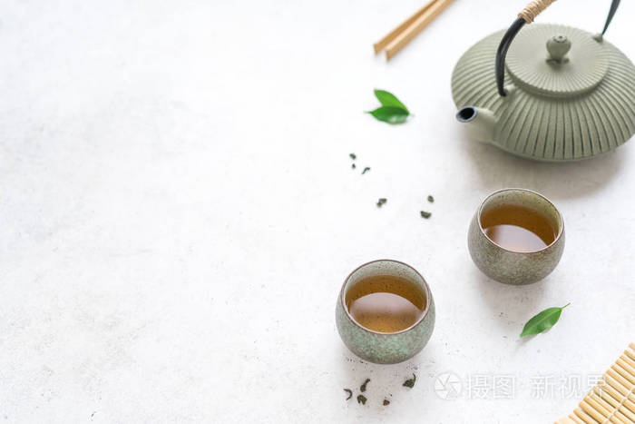 中国茶具铁茶壶和陶瓷茶杯与绿茶和叶子。 传统茶组合物在白色背景复制空间上。