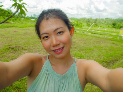 年轻快乐迷人的亚洲女性，在热带岛屿上用手机自拍，摆出愉快轻松的姿态，探索自然，享受假期旅行