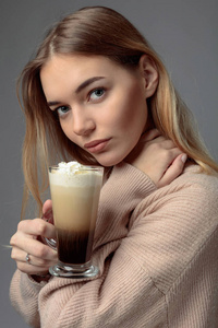 带着爱尔兰咖啡的迷人年轻女人。穿着毛衣的金发美女拿着一杯咖啡和奶油。