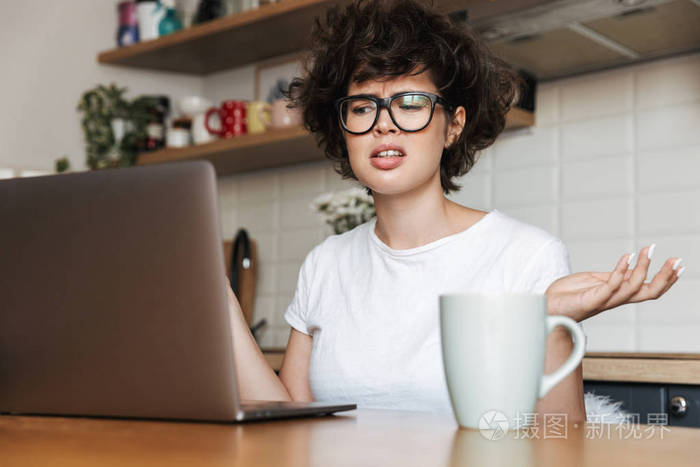 一位沮丧的年轻女性，戴着眼镜，早上在家里用笔记本电脑工作