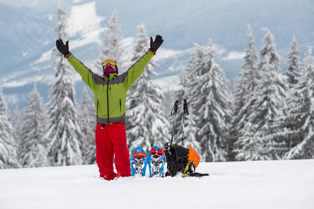 张开双臂的旅行者站在巨大松树的背景上，白雪覆盖在冬季旅行设备旁边。 史诗般的冬季冒险在山上。
