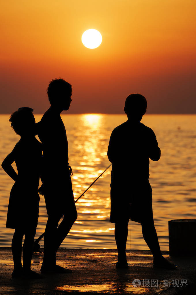 三个男孩在码头日落时钓鱼的剪影金色的大海和夕阳在