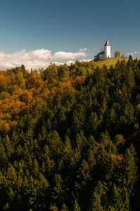 秋季，针叶林和落叶林混合斜坡，顶部有一座古老的基督教教堂