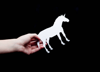 s hand holds a white unicorn with a black background paper.