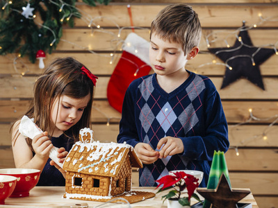 一位年轻的哥哥和姐姐在圣诞节前在家装饰姜饼屋的照片。