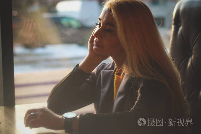 那个女孩坐在桌子旁的一家咖啡馆里,他的手支撑着他的脸颊.