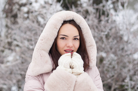 年轻美丽的情感女人的肖像，穿着带帽的羽绒衣和手套，在白雪覆盖的花园背景。冬季雪景