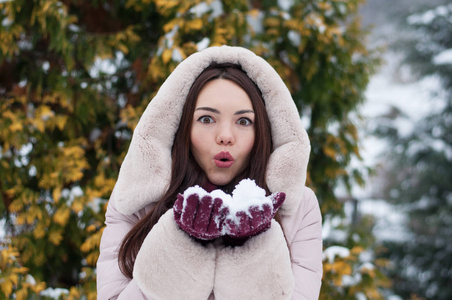 年轻美丽的情感女人的肖像，穿着带帽的羽绒衣和手套，在白雪覆盖的花园背景。冬季雪景