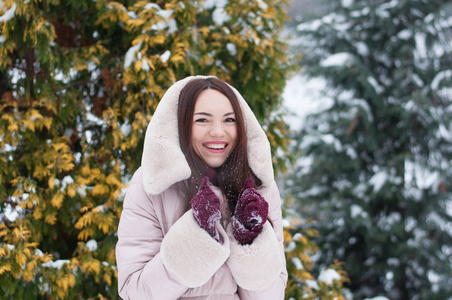 年轻美丽的情感女人的肖像，穿着带帽的羽绒衣和手套，在白雪覆盖的花园背景。冬季雪景