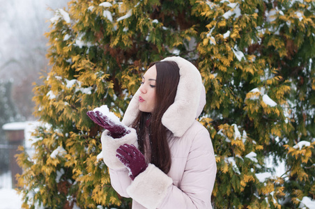 年轻美丽的情感女人的肖像，穿着带帽的羽绒衣和手套，在白雪覆盖的花园背景。冬季雪景