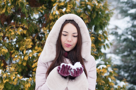 年轻美丽的情感女人的肖像，穿着带帽的羽绒衣和手套，在白雪覆盖的花园背景。冬季雪景