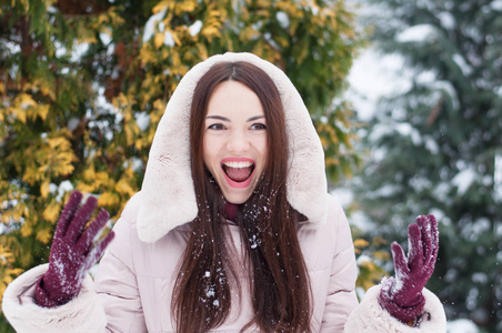 年轻美丽的情感女人的肖像，穿着带帽的羽绒衣和手套，在白雪覆盖的花园背景。冬季雪景