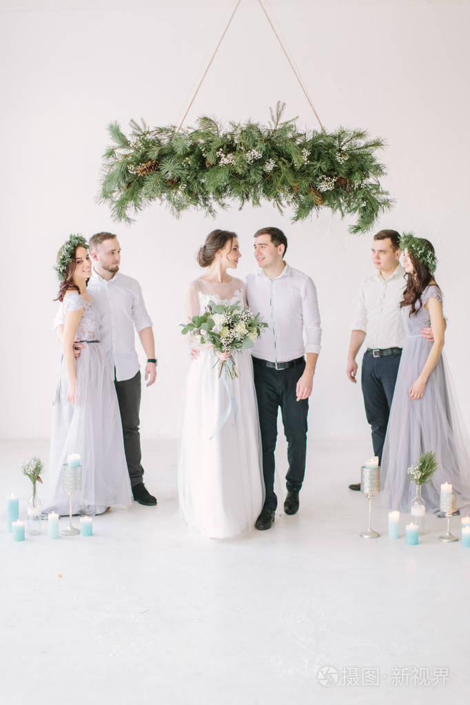 新婚快乐伴娘和伴郎在白色装饰的工作室里摆姿势