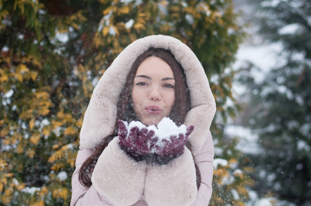 年轻美丽的情感女人的肖像，穿着带帽的羽绒服和手套，在白雪覆盖的花园背景上。 冬季雪景