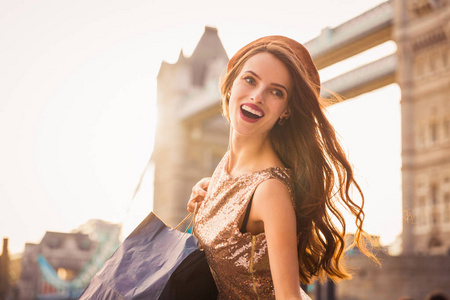一位微笑的年轻女子的肖像，她站在桥的背景下，手里拿着购物袋