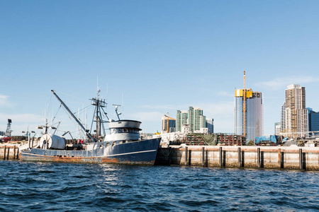 一艘渔船停靠在圣迭戈加州港口的一个码头上，背景是市中心的天际线。