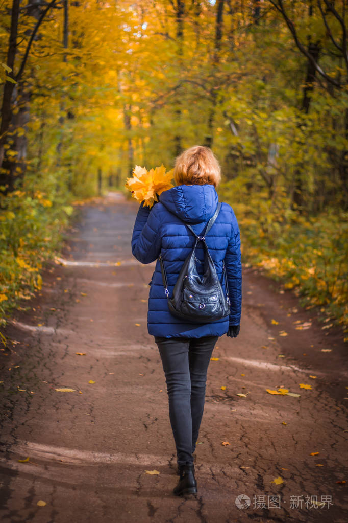秋天的森林里有一个带着一束秋叶的女人在路上照片-正版商用图片15ia