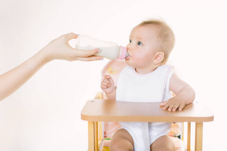 s hand feeds the baby out of the bottle. The child is seated in 