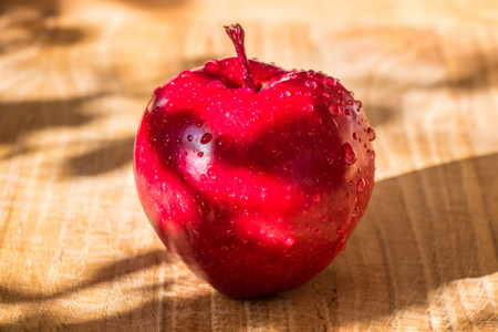 朱红色的苹果在木桌上，上面有水滴。 非常美味和新鲜的苹果投下阴影。