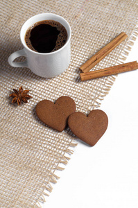 两个生姜饼干形状的心杯咖啡肉桂和八角星在粗糙的织物上位于白色背景。