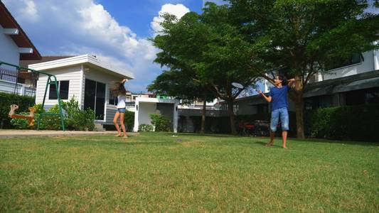 一个十几岁的男孩和女孩在他们家后院的绿色草坪上打羽毛球。