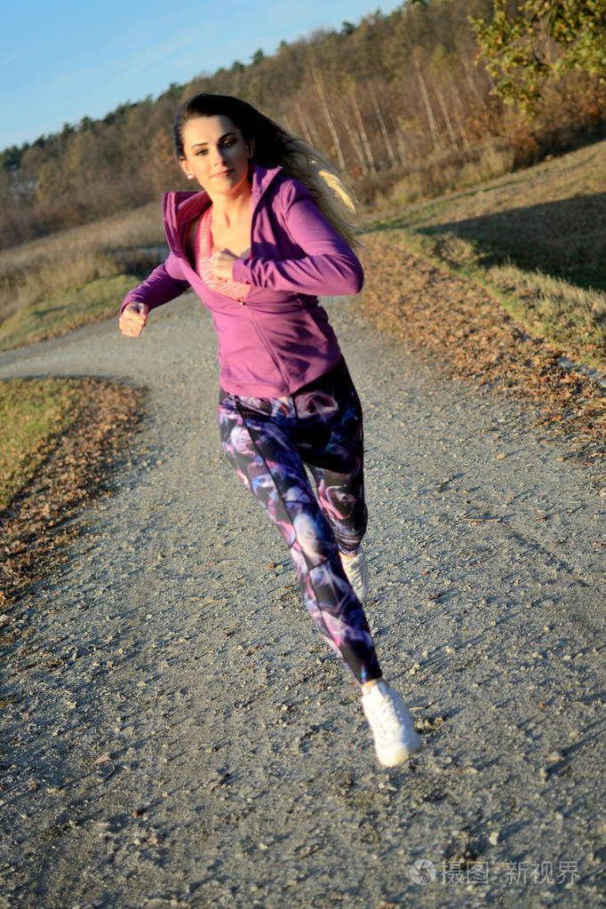在森林里奔跑的少女金发女性五颜六色的紧身裤和紫色的上衣活跃的跑步