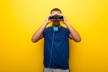美国黑人男子,黄色背景蓝色t恤,用望远镜在远处寻找东西照片