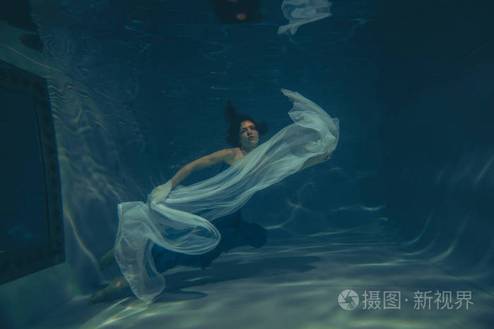 优雅漂亮的女人在水下游泳,就像一个独自穿着蓝色晚礼服的自由潜水员