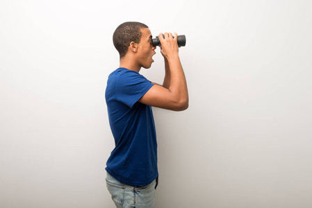 年轻的非裔美国人，穿着白色的墙，用望远镜看远处