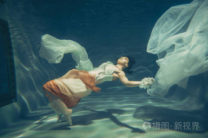优雅苗条的女孩在水下游泳就像一个自由潜水员穿着白色的晚礼服和美丽