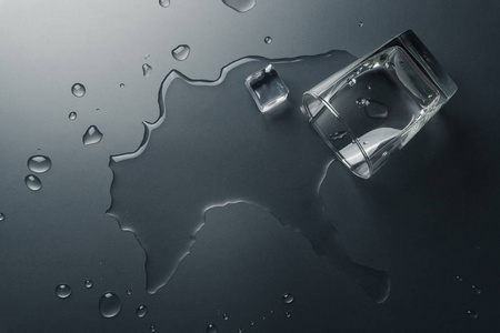 一杯冰块洒在桌子上的水的俯视图照片