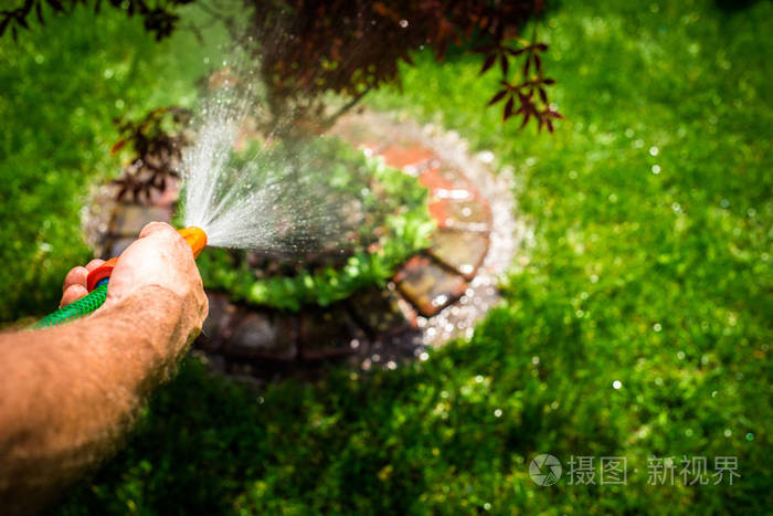 那个人正在花园里浇水. 一个男人拿着外套的景色. 节约植物的用水.