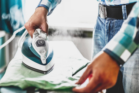 s clothes. Man in role of a woman at home. Man ironing shirt on 