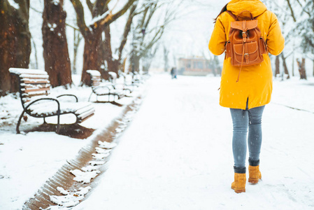 在下雪的城市公园散步的女人。 从后面看。 背包。 冬季概念