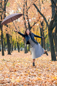 带着雨伞在秋天公园摆姿势的女人。 明亮的黄色叶子和树木。 她模仿风。
