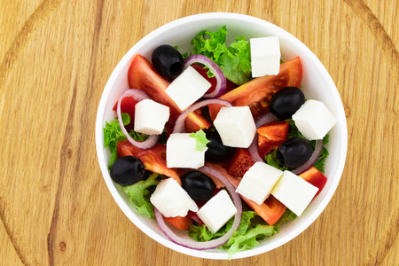 希腊沙拉与新鲜蔬菜，菲塔奶酪和黑色橄榄在木制背景。 上面的风景。