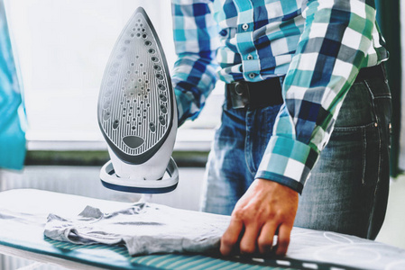 s clothes. Man in role of a woman at home. Man ironing shirt on 