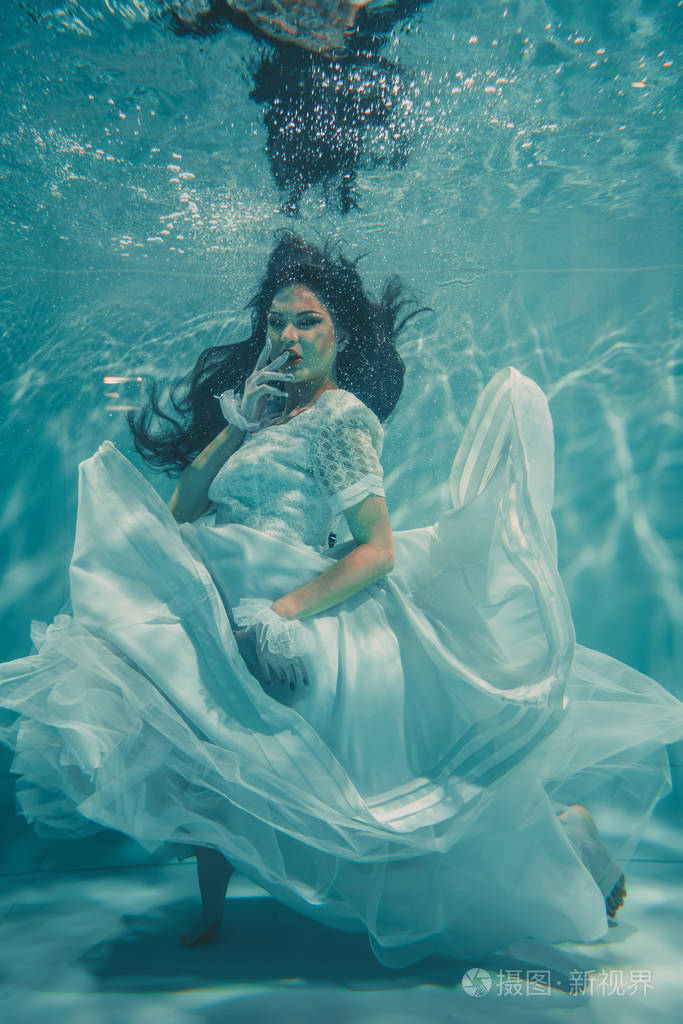 穿着白色婚纱在水下游泳的性感年轻新娘,长袜和手套