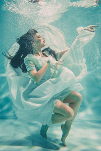 穿着白色婚纱在水下游泳的年轻新娘，长袜和手套