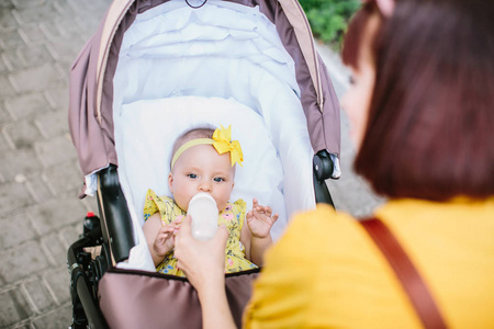 婴儿在马车中饮用牛奶的前景，母亲在户外春季或夏季用新鲜的绿色背景牵手。